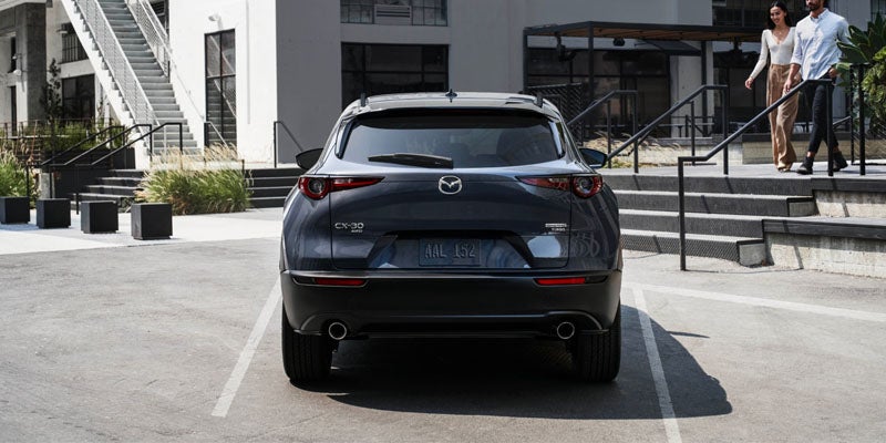 Rear view of a Mazda CX-30 parked in a marked parking space outside a modern residential or commercial building