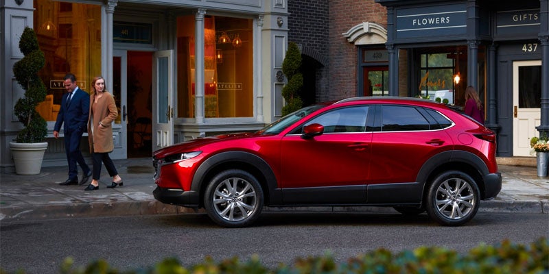 Red Mazda CX-30 crossover SUV parked along a city street in front of storefronts