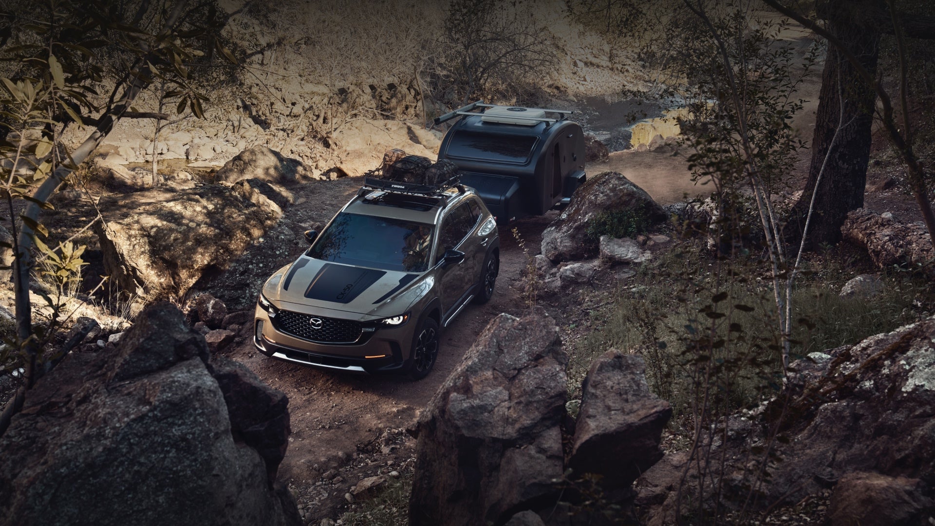 Mazda SUV towing an off-road camper trailer along a rugged rocky trail surrounded by large boulders