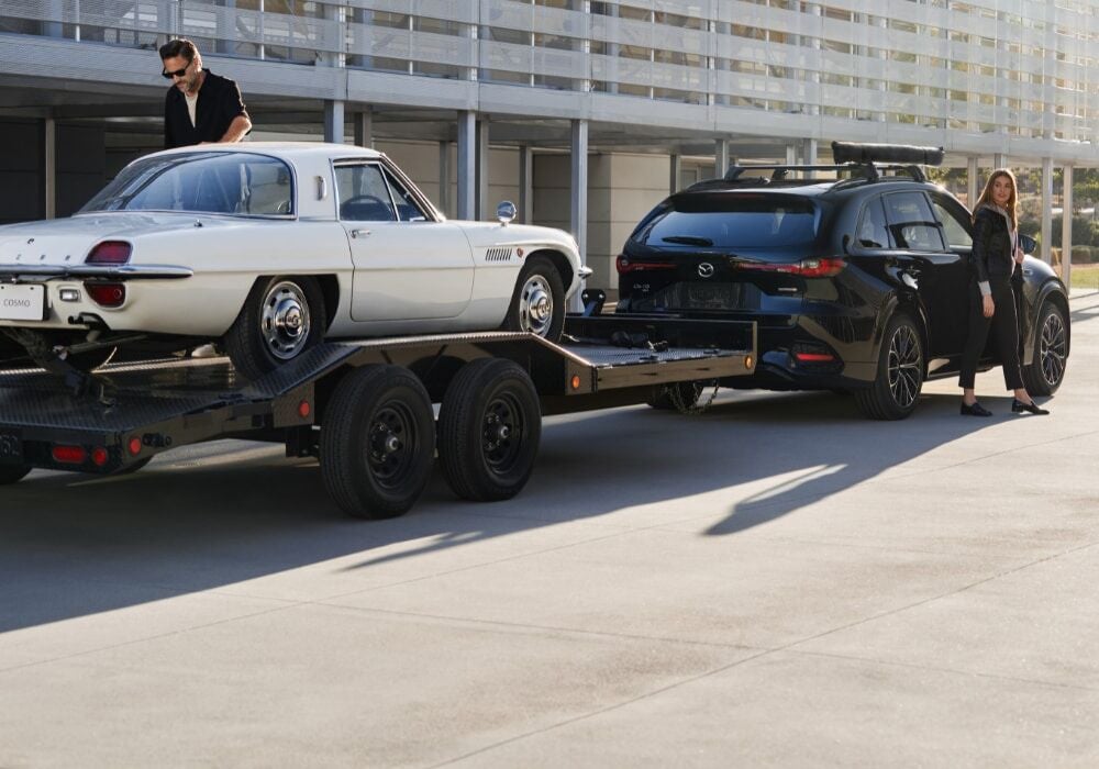 Black 2025 Mazda CX-70 towing a white sports car