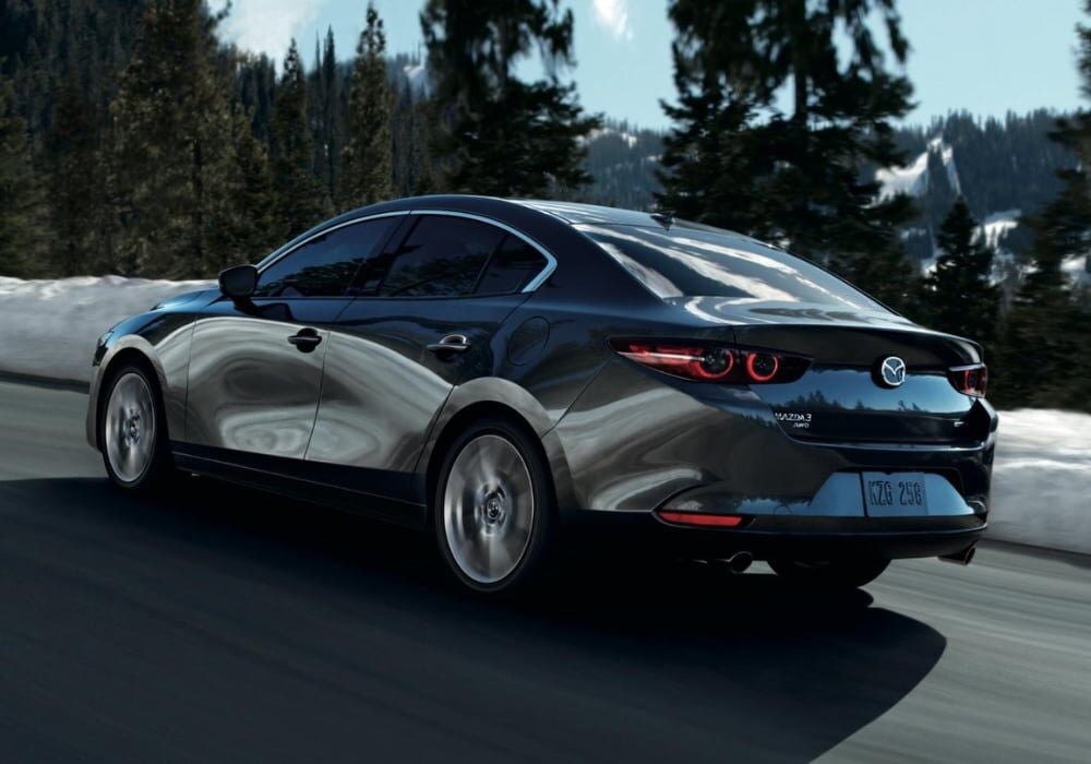 Rear view of a black 2026 Mazda3 sedan driving down a road