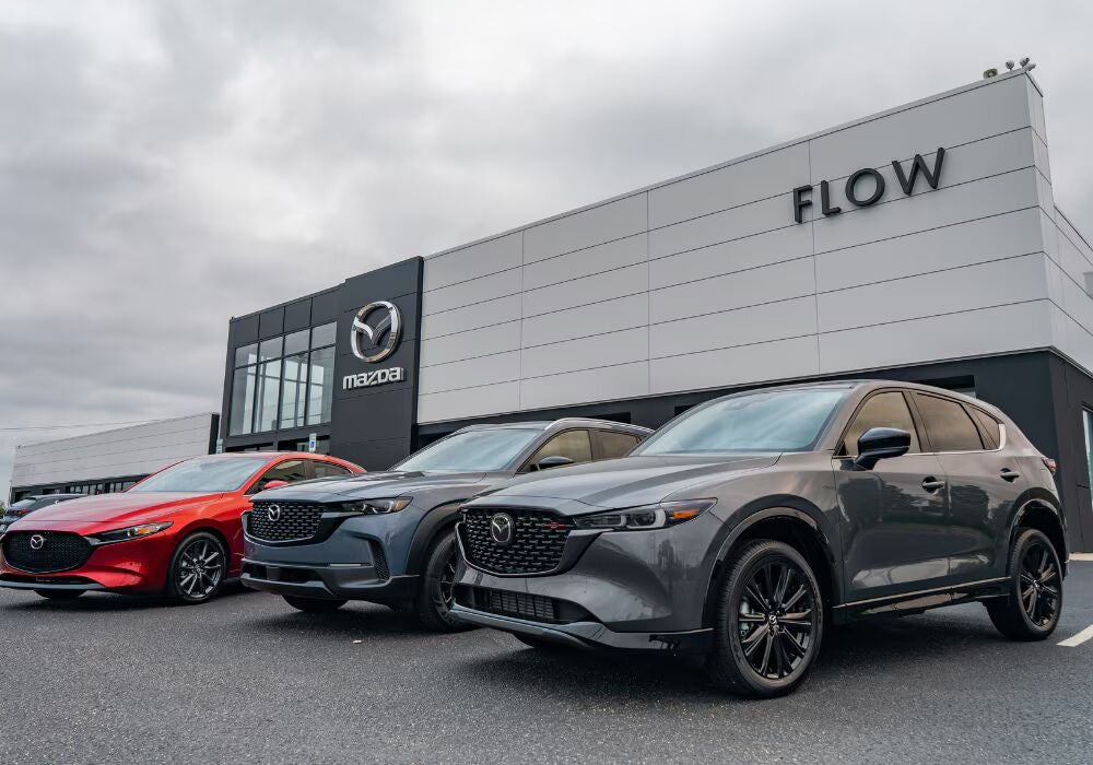 The storefront of the Flow Mazda of Fayetteville dealership with three Mazda SUVs parked in front of…