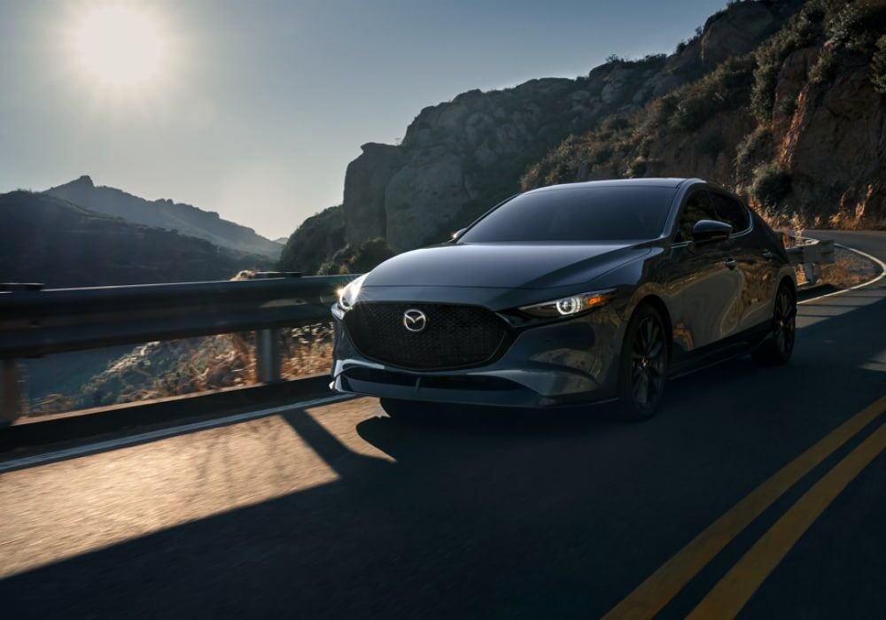 2025 Mazda3 driving down a road with mountains in the background