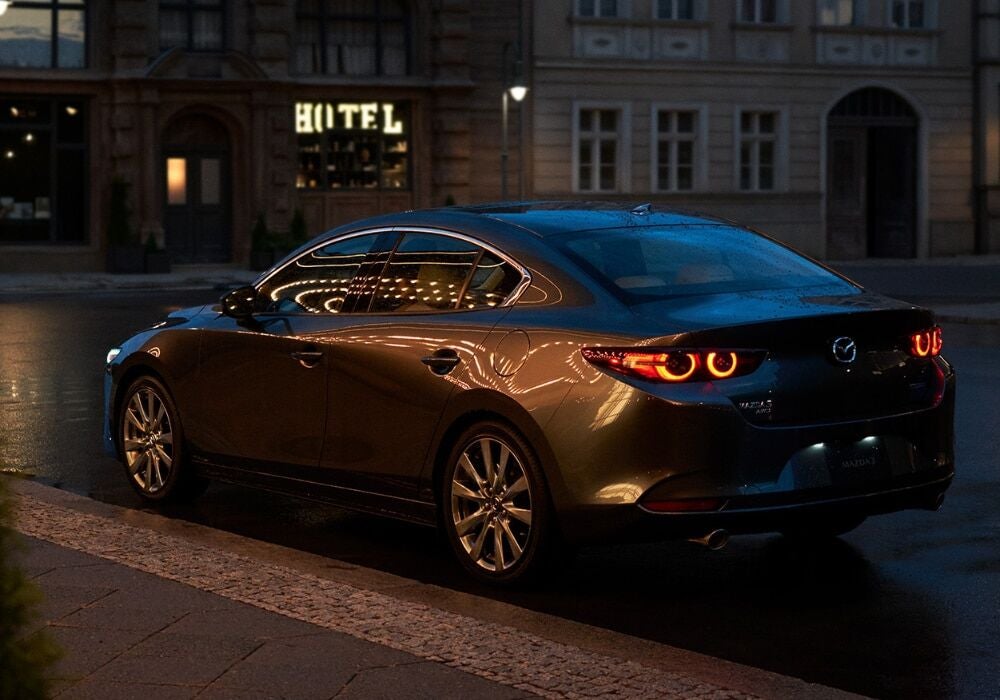 Mazda3 sedan parked on a city street. There are streetlights being reflected on the body of the car